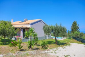A house with a tiled roof, a small garden with various plants, and a clear blue sky.