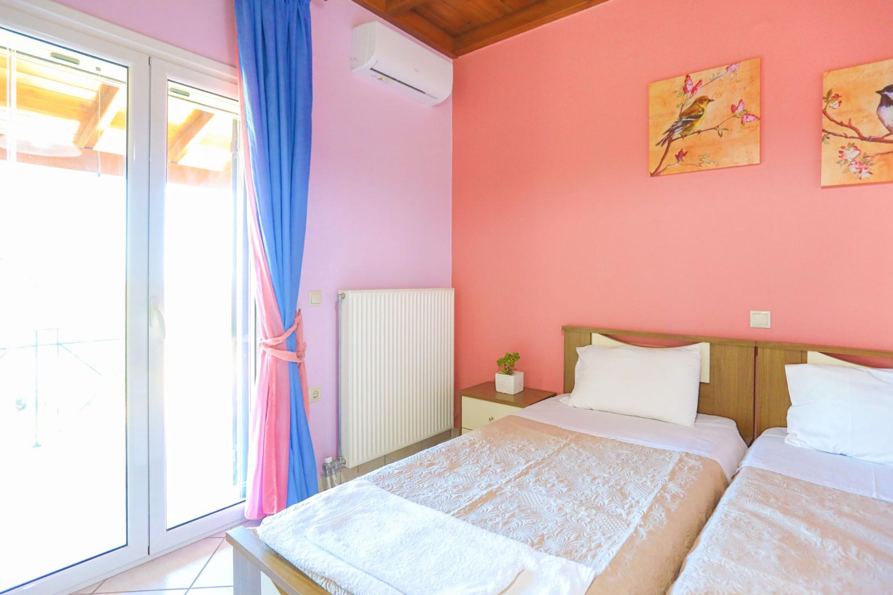 Camera da letto con due letti, una finestra con tende, un termosifone e due quadri appesi al muro raffiguranti uccelli.
