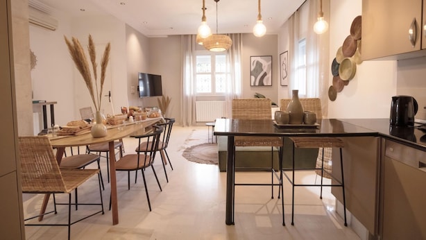 A modern kitchen with a dining area, featuring a long wooden table, wicker chairs, and pendant lights. - Villa Bord de mer Piscine Chauff e et Terrasse (La Marsa)