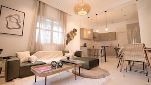 A modern living room with a sofa, coffee table, and dining area. There is a kitchen in the background with cabinets and a dining table. - Villa Bord de mer Piscine Chauff e et Terrasse (La Marsa)