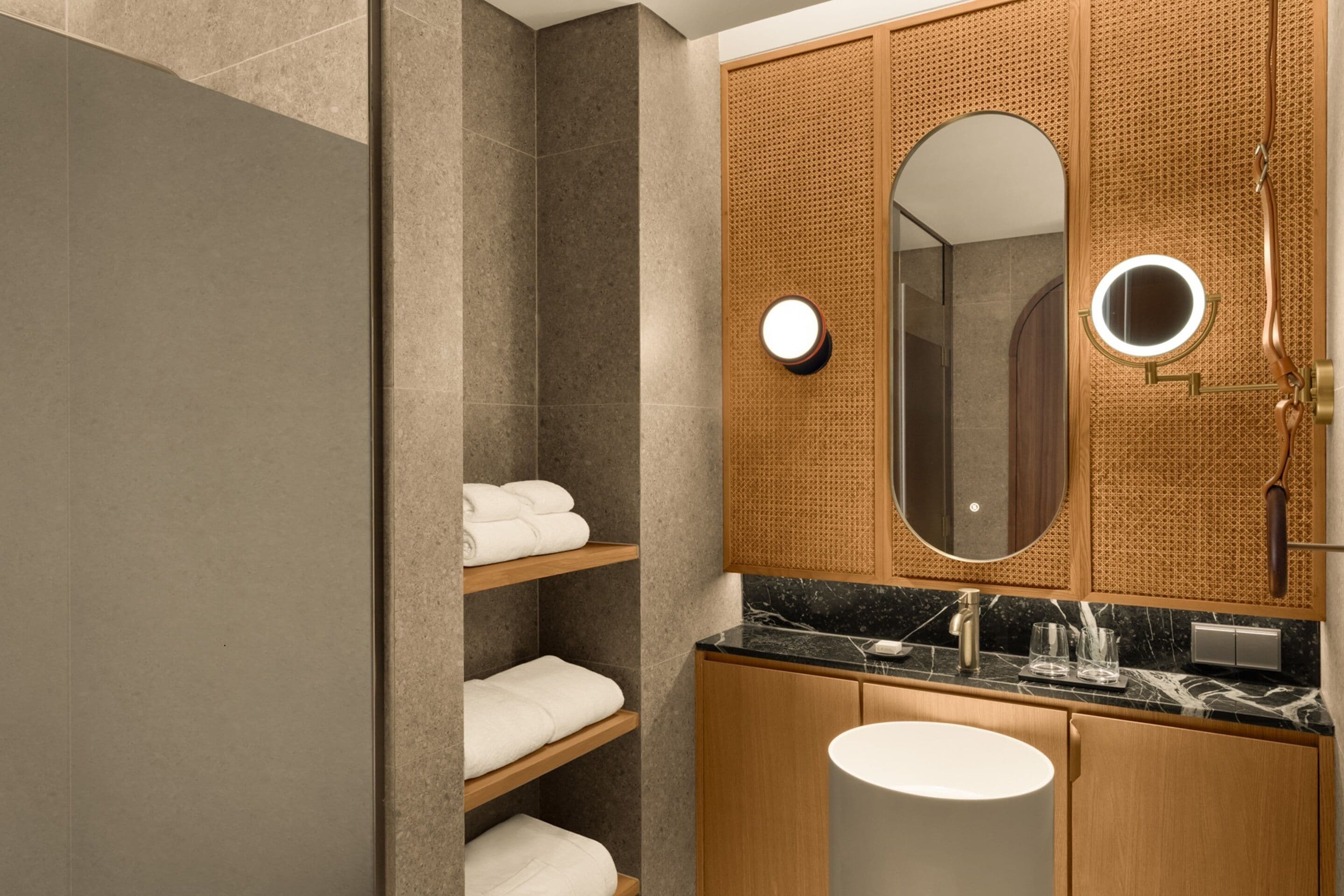 A modern bathroom with a large mirror, wooden shelves with towels, a sink, and a shower area.