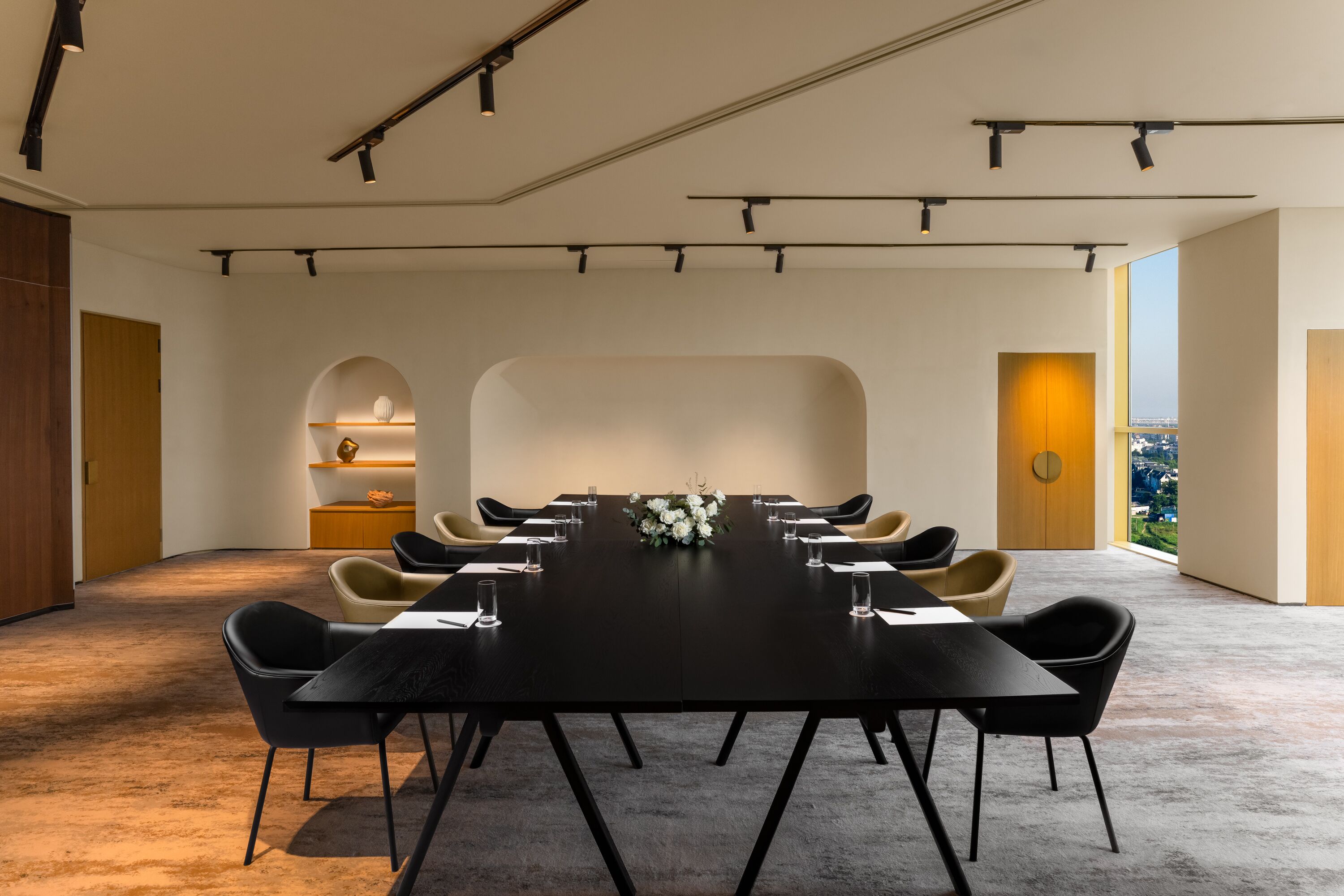 Una sala de conferencias moderna con una larga mesa, sillas negras y un jarrón de flores blancas.