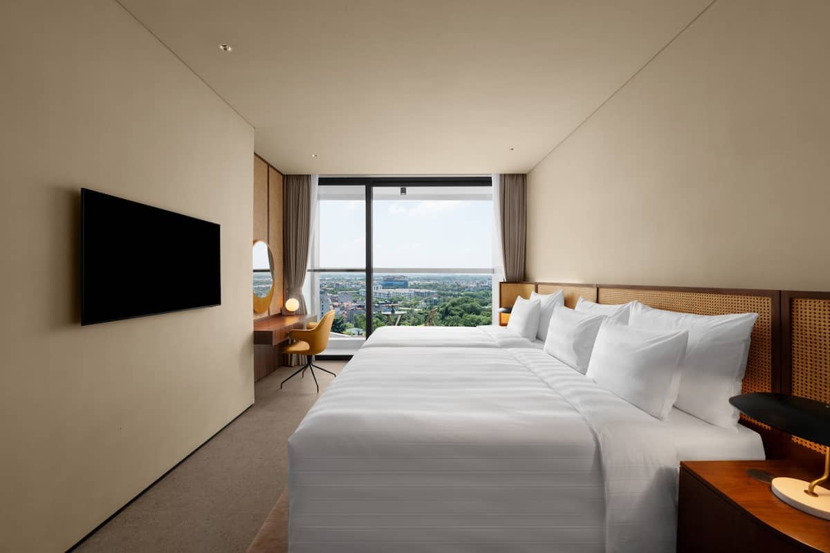 Habitación de hotel con una cama grande, un escritorio, una silla, un televisor y vistas a la ciudad.
