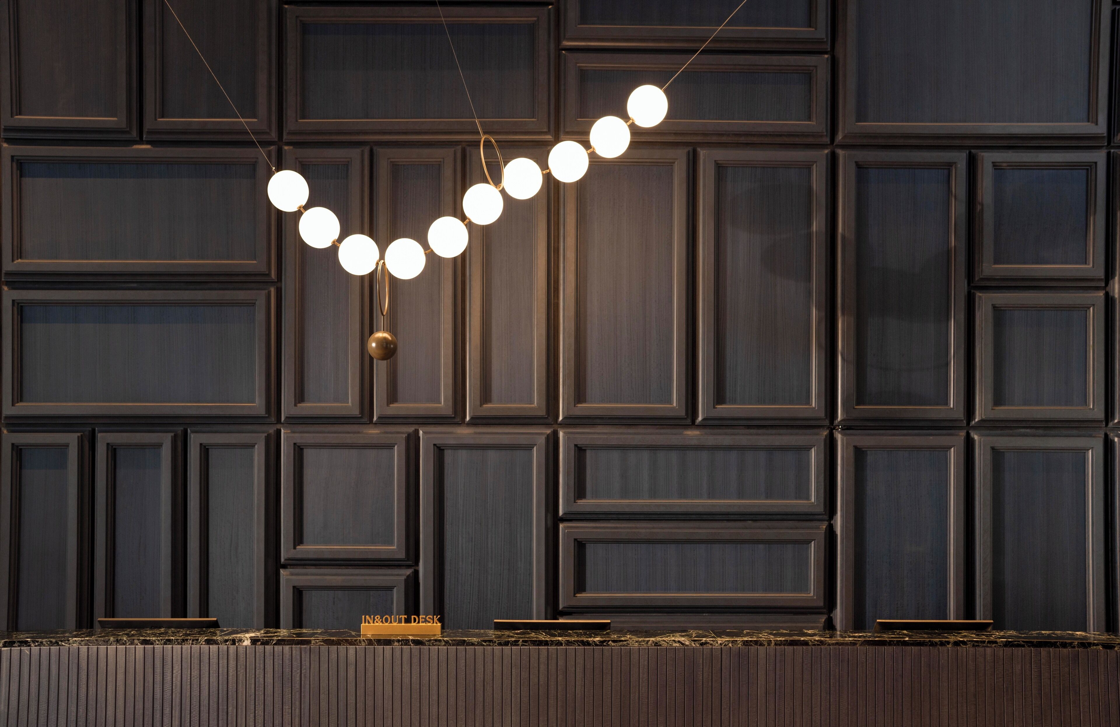 A modern interior with a dark wood panel wall and a pendant light with multiple bulbs.