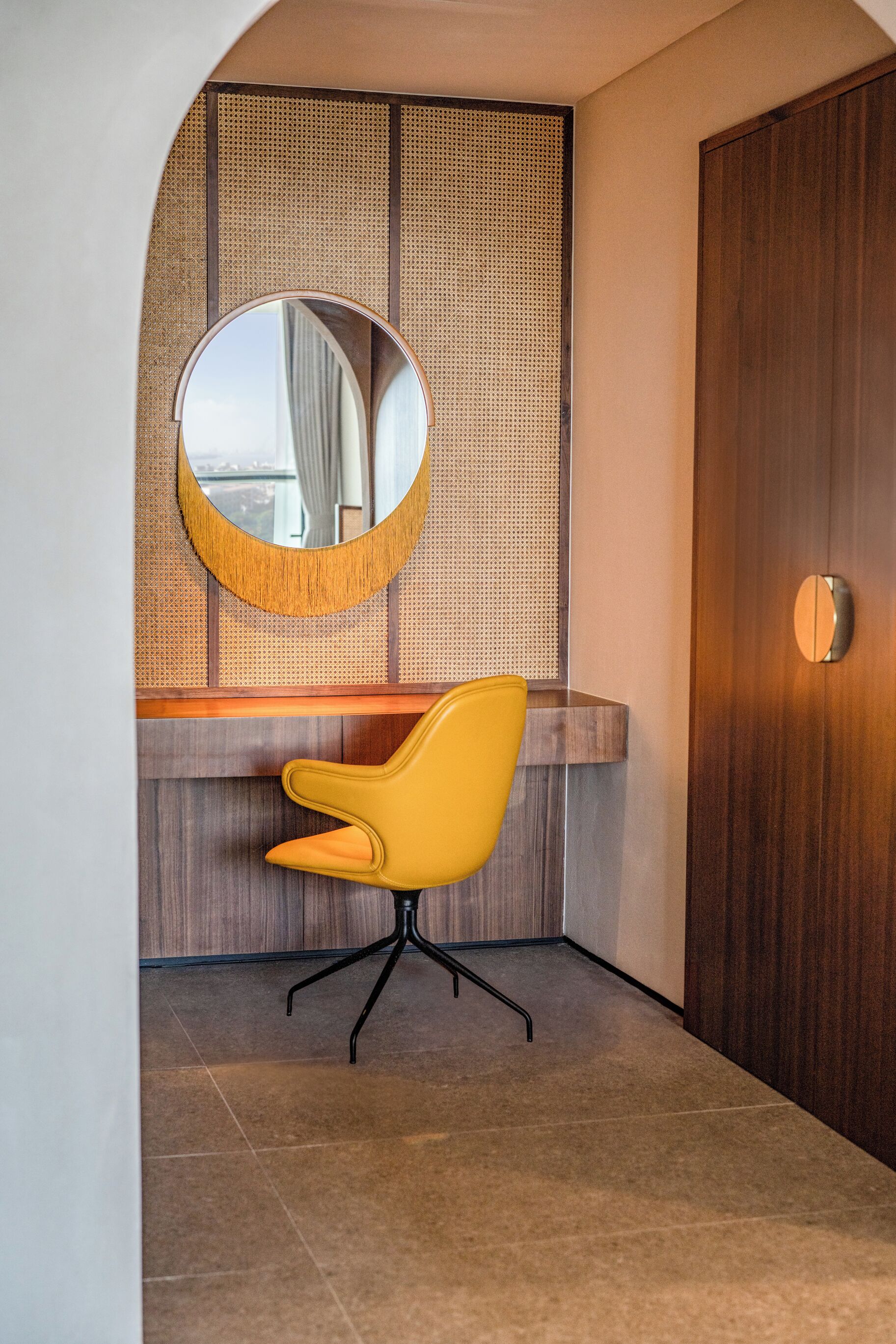 A modern bathroom with a round mirror, yellow chair, wooden vanity, and a large wooden door.