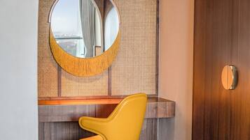 A modern bathroom with a round mirror, yellow chair, wooden vanity, and a large wooden door.