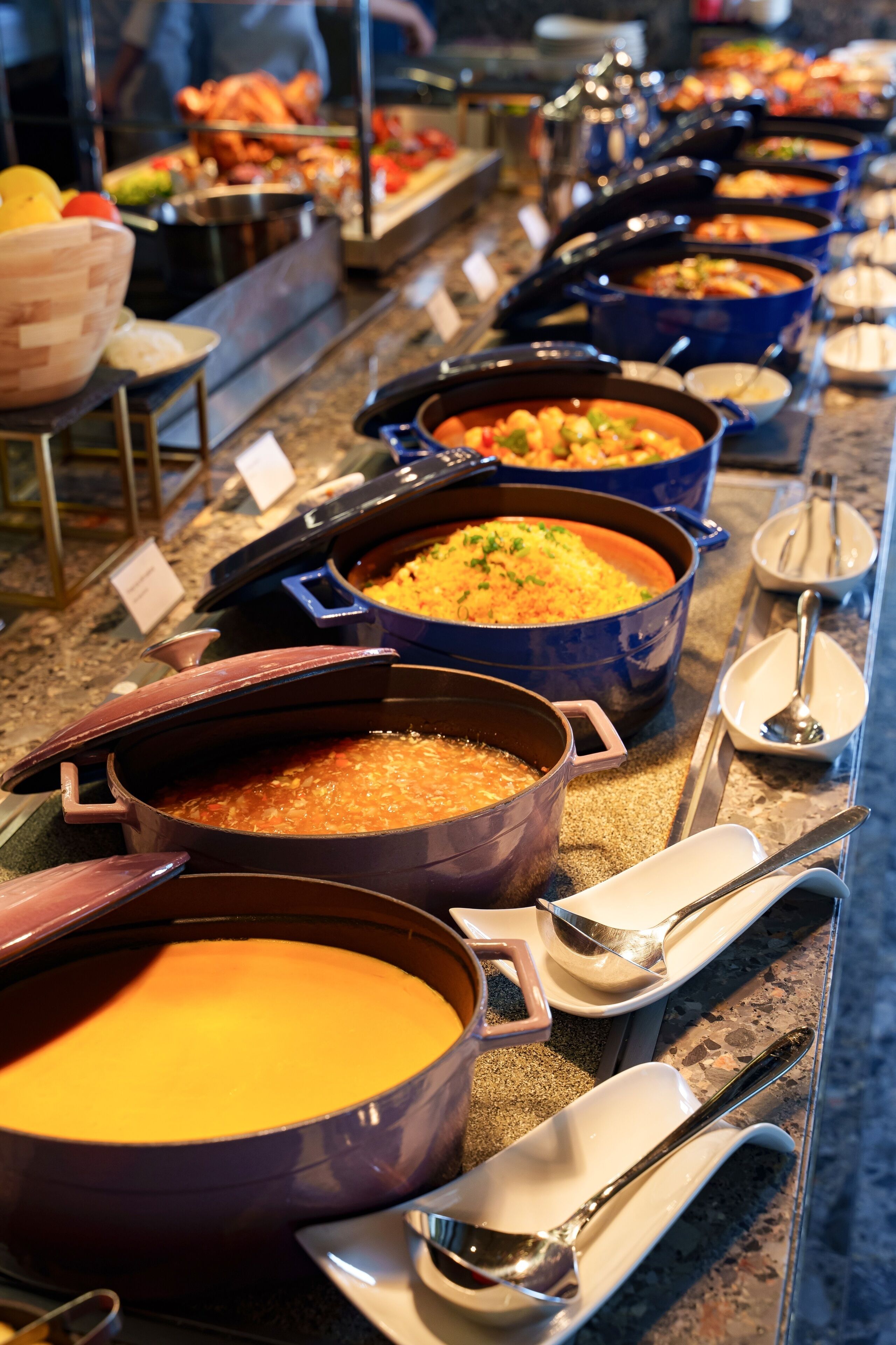 A buffet with various dishes in large pots, arranged on a counter with serving utensils and plates.