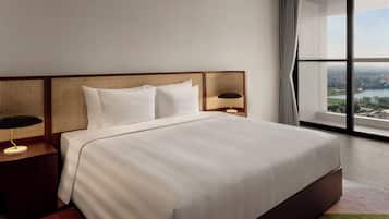 A modern hotel room with a large bed, a nightstand with a lamp, and a view of a cityscape through a large window.