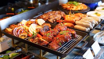 Un buffet proposant une variété de plats, notamment des viandes grillées, des saucisses et des légumes.