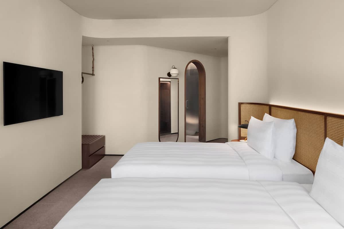 Una habitación de hotel con una cama grande, un televisor montado en la pared, una mesita de noche de madera y una puerta que da a un baño.
