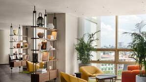 A modern living room with a large window, a bookshelf, and a seating area with a yellow sofa and orange ottoman. - L7 WEST LAKE HANOI By LOTTE HOTELS (Hanoi)