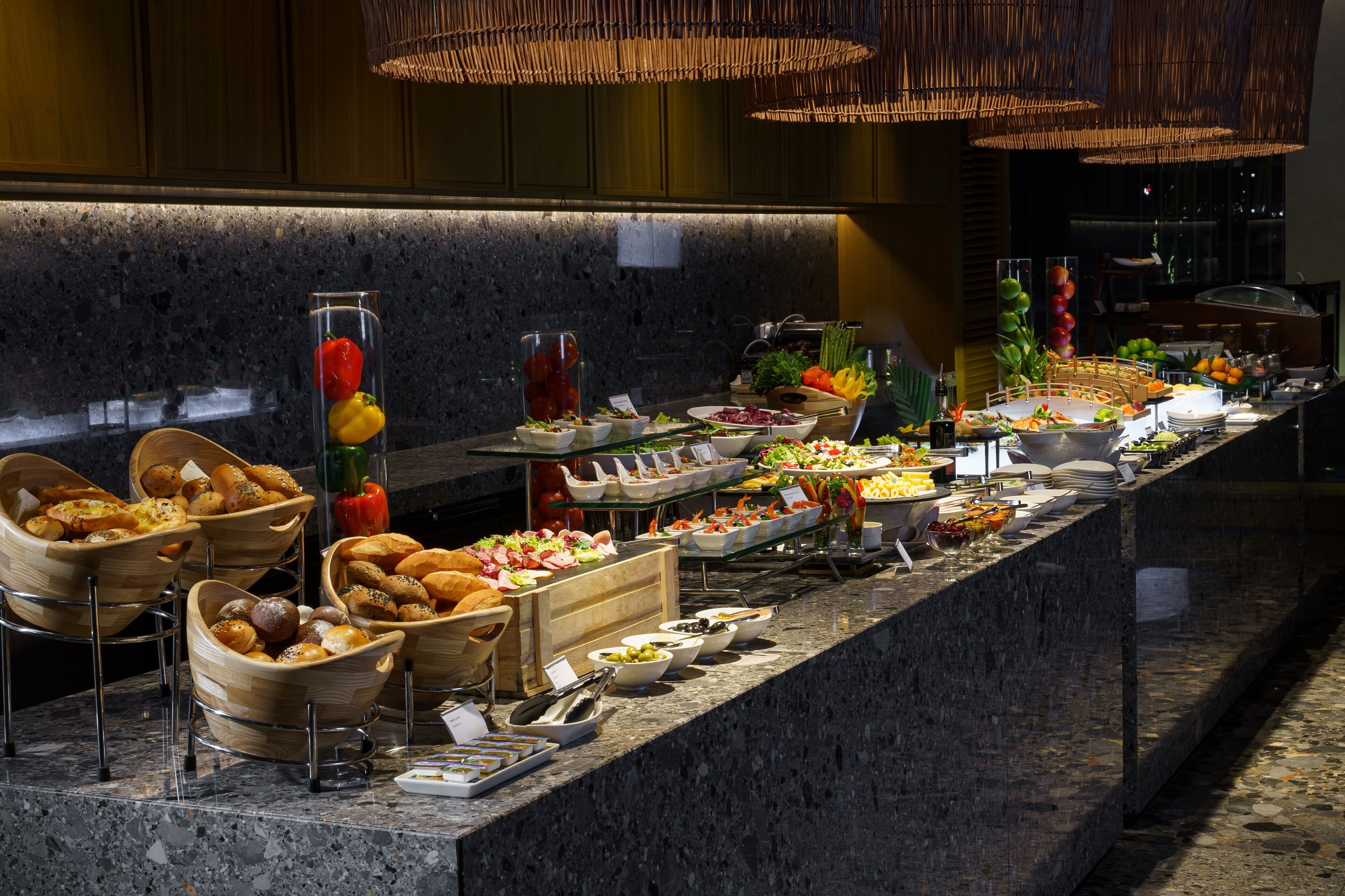 A buffet with various food items and drinks, including fruits, vegetables, and baked goods, arranged on a marble counter.