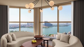A modern living room with a sofa set, a coffee table with fruit, and a view of a cityscape through large windows. - L7 WEST LAKE HANOI By LOTTE HOTELS (Hanoi)