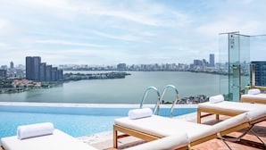 A rooftop infinity pool with lounge chairs and a glass enclosure, overlooking a cityscape and a body of water. - L7 WEST LAKE HANOI By LOTTE HOTELS (Hanoi)
