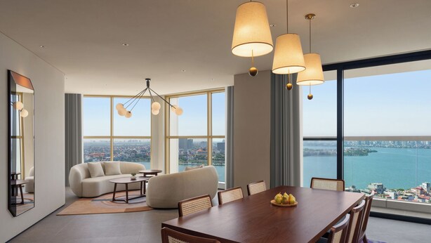 A modern dining area with a wooden table and chairs, a sofa, and a city view through large windows. - L7 WEST LAKE HANOI By LOTTE HOTELS (Hanoi)