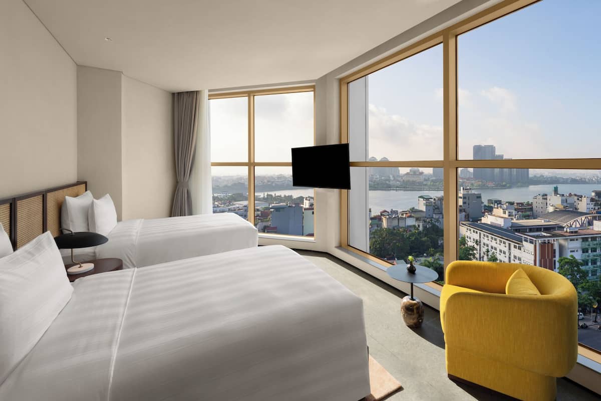 Habitación de hotel con dos camas, un televisor y un ventanal grande con vistas a la ciudad.