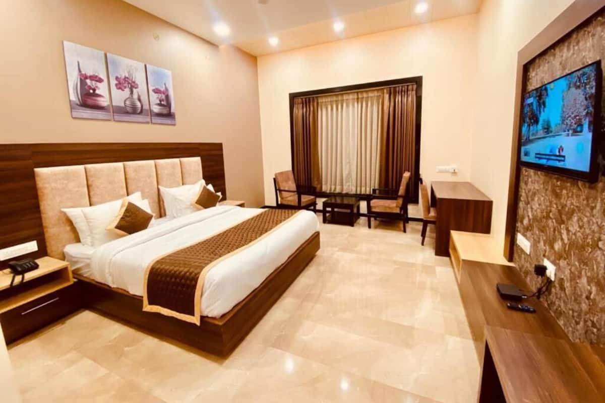 A hotel room with a large bed, a desk, a chair, and a TV on the wall.