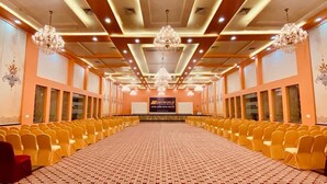 A conference room with rows of yellow chairs, a patterned carpet, chandeliers, and a banner with text. - SKYWORLD Hotels and Resorts (Kuchaman)