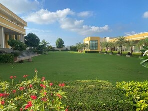 A courtyard with a lawn, potted plants, and a building with a yellow facade and large windows. - SKYWORLD Hotels and Resorts (Kuchaman)