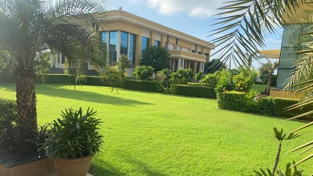 A well-maintained courtyard with a lawn, potted plants, and a modern building in the background. - SKYWORLD Hotels and Resorts (Kuchaman)