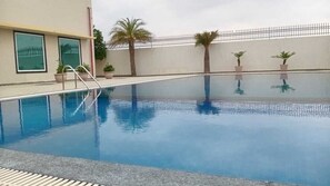 A swimming pool with a metal ladder, surrounded by potted plants and a fence. - SKYWORLD Hotels and Resorts (Kuchaman)