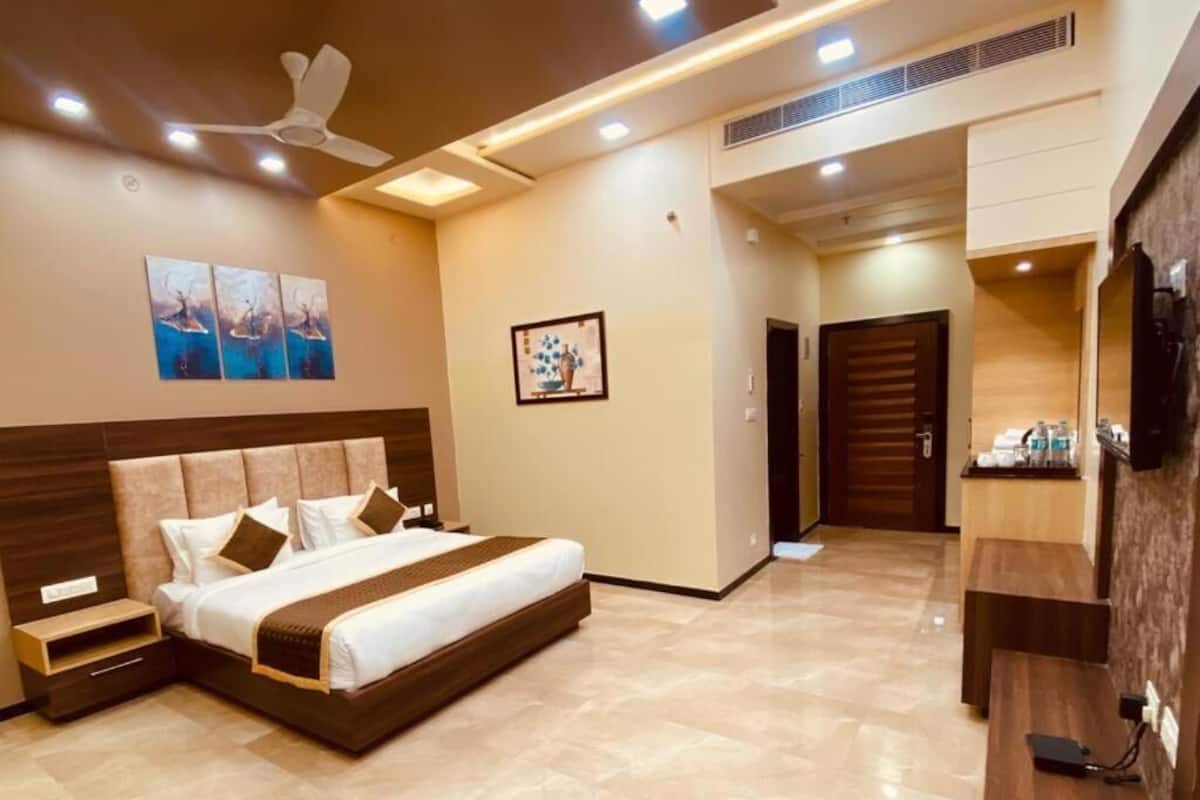 A modern hotel room with a large bed, a ceiling fan, recessed lighting, a TV, and a small desk.