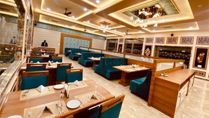 A restaurant with multiple seating areas, including booths and tables, with a marble floor and ceiling with recessed lighting. - SKYWORLD Hotels and Resorts (Kuchaman)