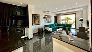 A modern living room with a green sofa, a coffee table, and a kitchen area with black countertops. - Gammarth Touristique Piscine Commune Bord de mer (La Marsa)