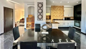 A modern dining area with a long table, chairs, and a decorative wall with clocks. - Gammarth Touristique Piscine Commune Bord de mer (La Marsa)