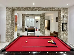 A pool table with a red felt surface, a single white cue ball, and a set of pool cues. - Gammarth Touristique Piscine Commune Bord de mer (La Marsa)
