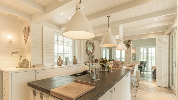 Una cocina amplia con armarios blancos, una isla grande con encimera de madera, iluminación colgante y vistas al comedor.