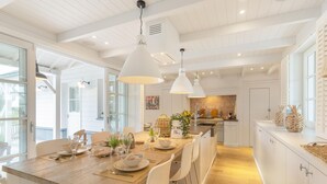 Cocina moderna con armarios blancos, una isla de madera, iluminación colgante y vistas al jardín trasero.