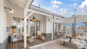 Un patio techado al aire libre con mobiliario de madera, una mesa dispuesta para comer y un paraguas grande que proporciona sombra.