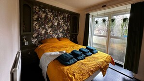 Een hotelkamer met een groot bed, bloemen behang en uitzicht op het landschap door een raam.