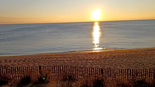 Una playa con una valla de madera al frente y el sol reflejado en el agua.
