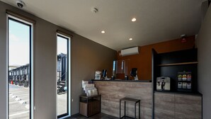 A modern interior with a reception desk, a coffee machine, and a view of the parking area through a glass door. - HOTEL R9 The Yard Fukuyama (Fukuyama)