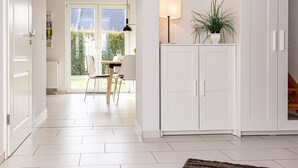 Una habitación luminosa y moderna con paredes y piso blancos, una zona de comedor con mesa y sillas, una lámpara y una planta en maceta.