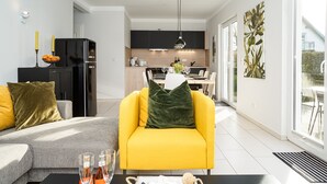 Una sala de estar moderna con un sofá amarillo, un sofá gris y una mesa de centro negra con botellas de vino.