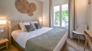 A neatly arranged bedroom with a large bed, bedside lamps, a chair, and a view of greenery outside. - Rêves de Provence 1 renovated vacation apartment Sea and beach 150 m away (Gassin)
