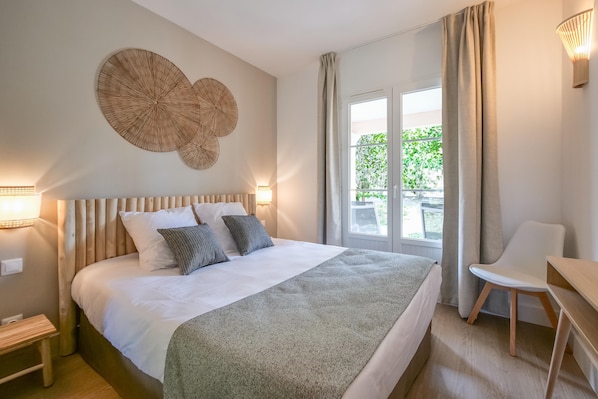 A neatly arranged bedroom with a large bed, bedside lamps, a chair, and a view of greenery outside.