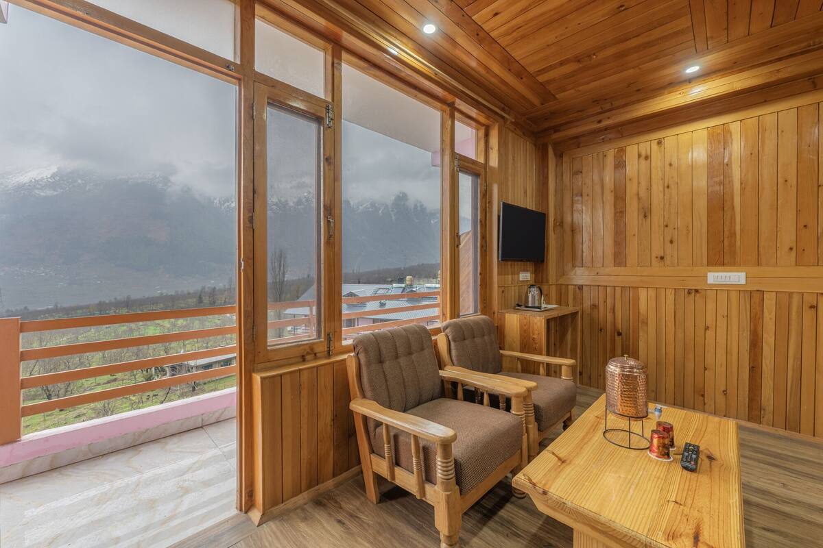 Una cabaña de madera con dos sillas y una mesa, grandes ventanales que ofrecen vistas a un paisaje nevado.