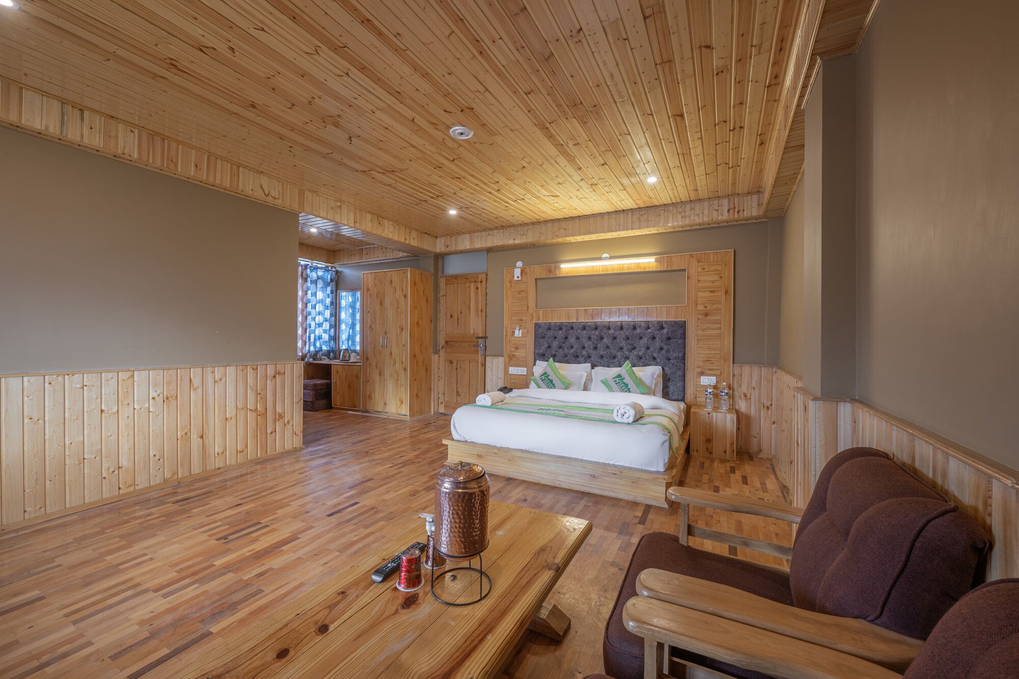 A wooden-paneled room with a bed, a small table with a kettle, and a chair.