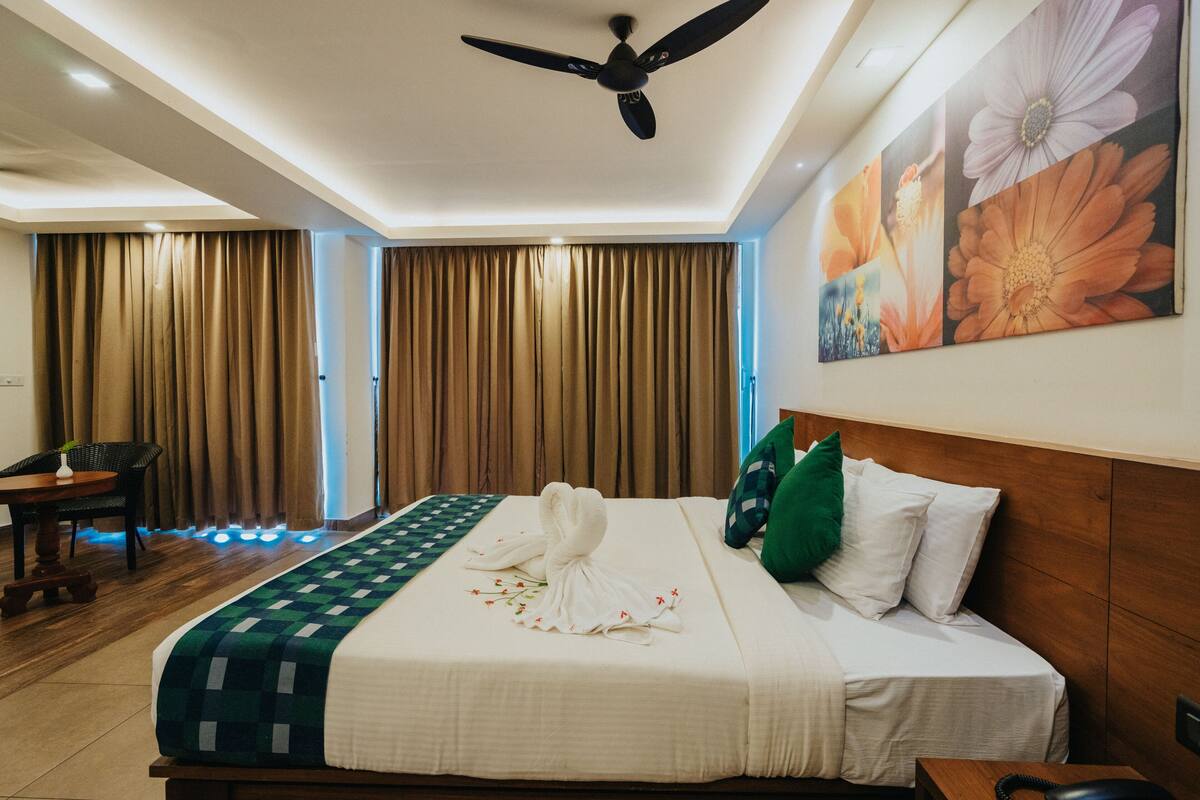 A hotel room with a bed, a ceiling fan, a desk with a chair, and curtains.