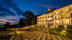 Ein mehrstöckiges Hotel mit gut beleuchtetem Eingang, gepflasterter Auffahrt und angelegtem Garten.
