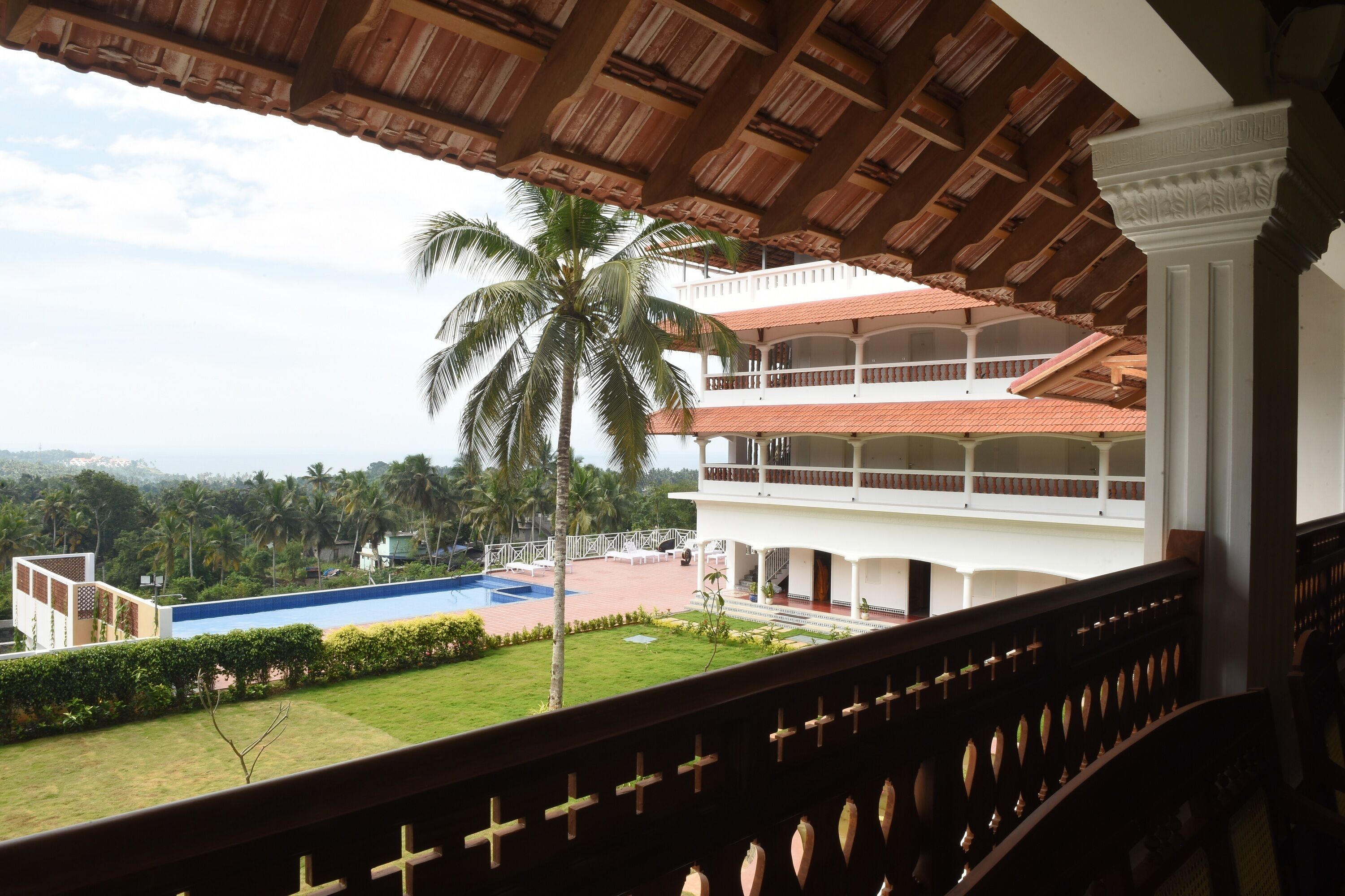 A balcony with a view of a pool, palm trees, and a multi-story building with a red roof.