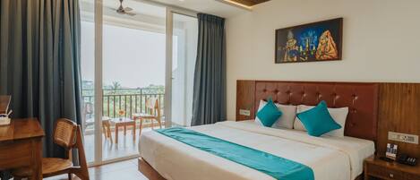 A hotel room with a large bed, a desk, and a balcony with a view.