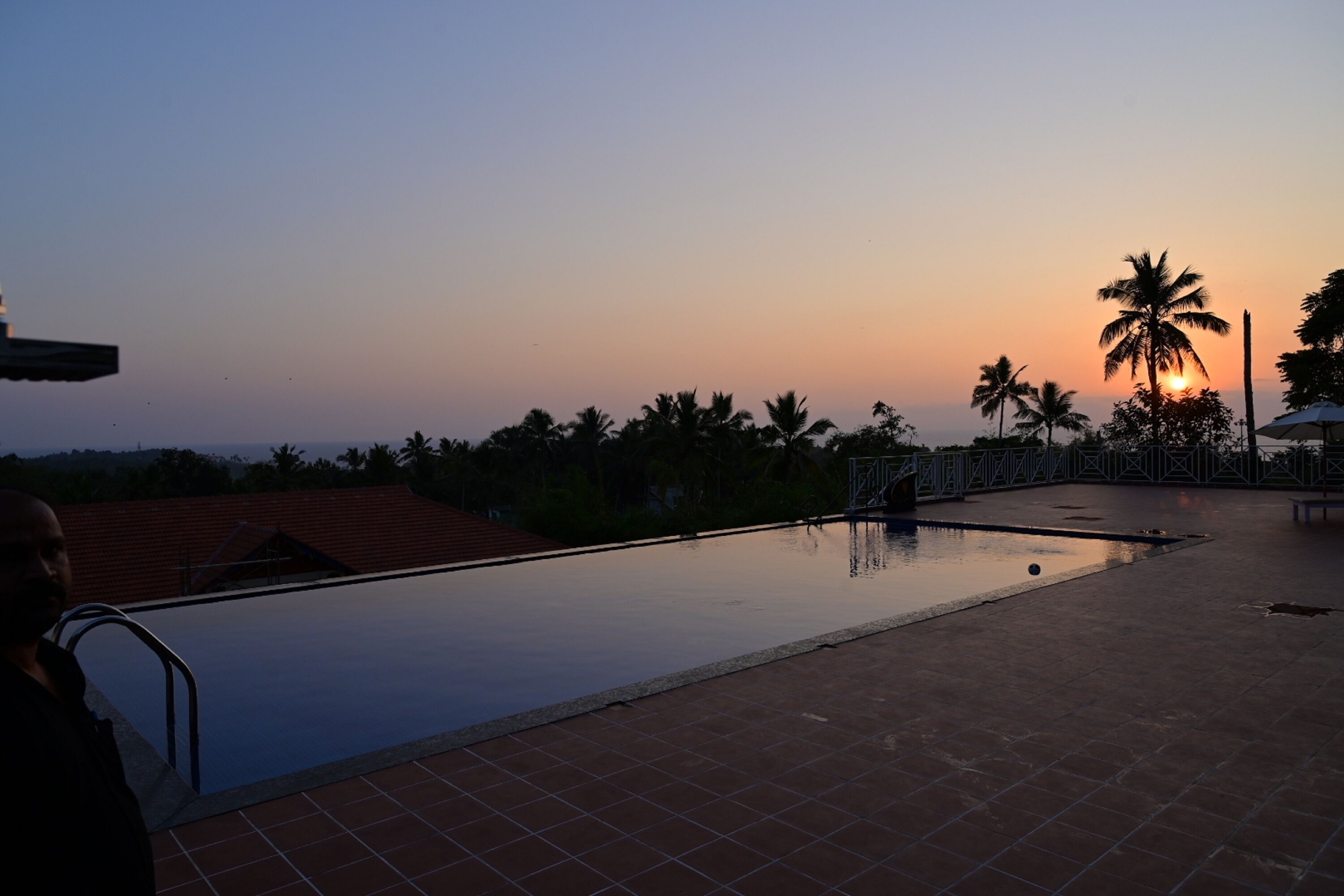 An outdoor swimming pool with a view of the sunset and palm trees.