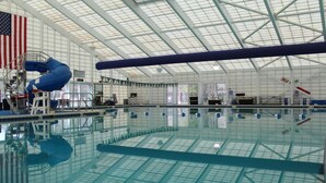 Une piscine intérieure avec un plafond haut, un drapeau américain et un toboggan bleu.