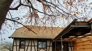 A traditional half-timbered building with a sloped roof, a covered outdoor seating area, and a staircase leading to the entrance. - Peaceful house in the heart of Alsace (Baldenheim)