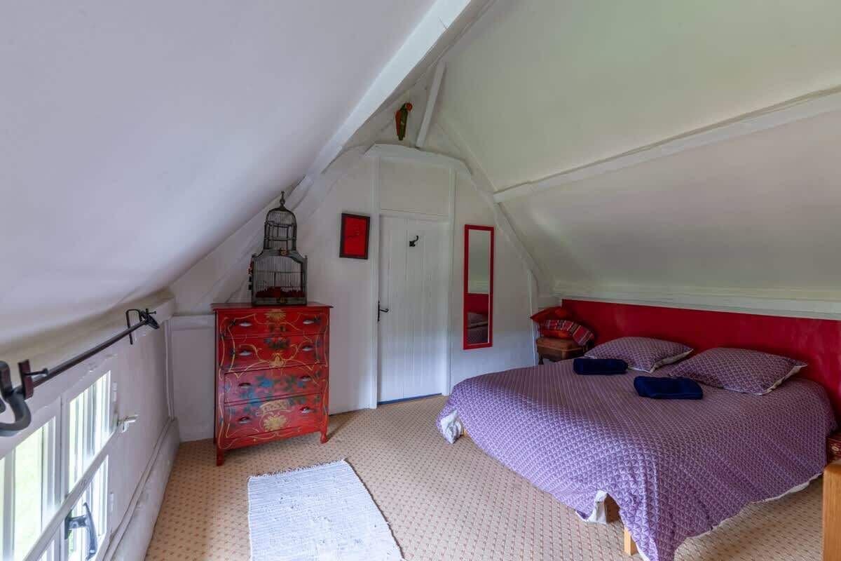 A bedroom with a sloped ceiling, a red dresser, a bed with purple bedding, and a white door.